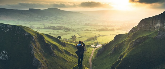 Person photographing a valley landscape at sunrise