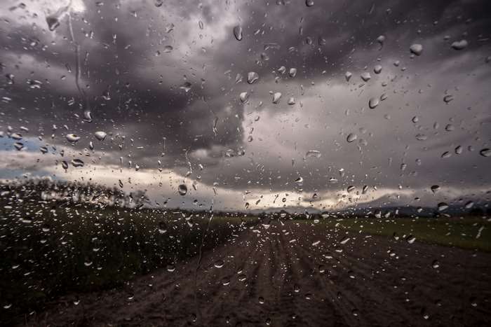 Raindrops on glass with stormy sky and landscape