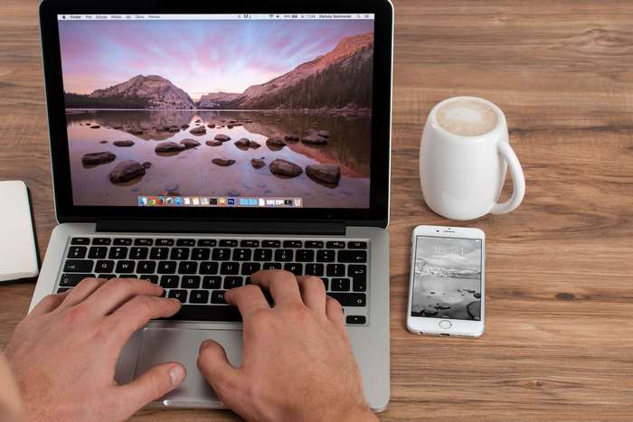 Person typing on MacBook Pro next to iPhone and coffee mug