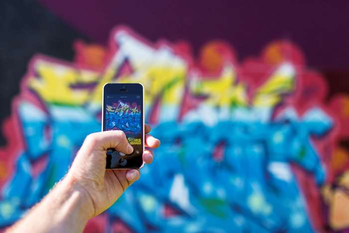 Hand holding iPhone taking a photo of graffiti art