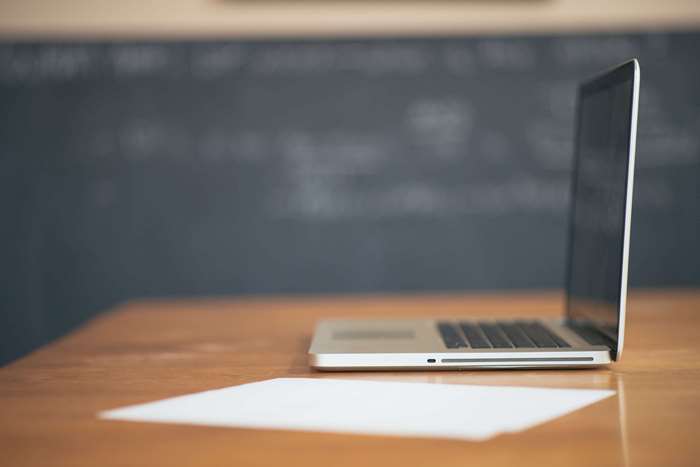 Apple MacBook on a wooden desk with a sheet of paper