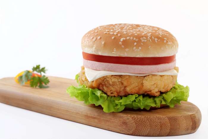 Chicken burger with lettuce and tomato on a wooden board
