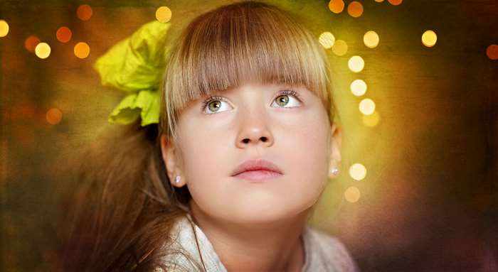 Young girl with bangs and a green bow looking up, bokeh lights