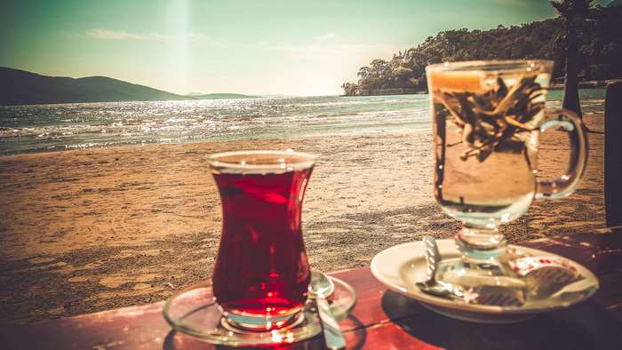 Two cups of tea on a beach with the ocean in the background