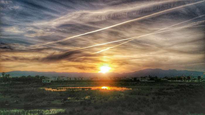 Sunset sky with contrails over mountains and water