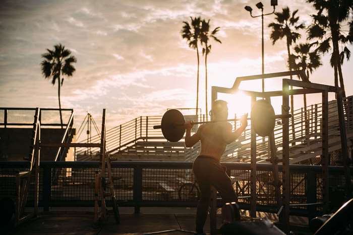 Man lifting weights at outdoor gym with palm trees
