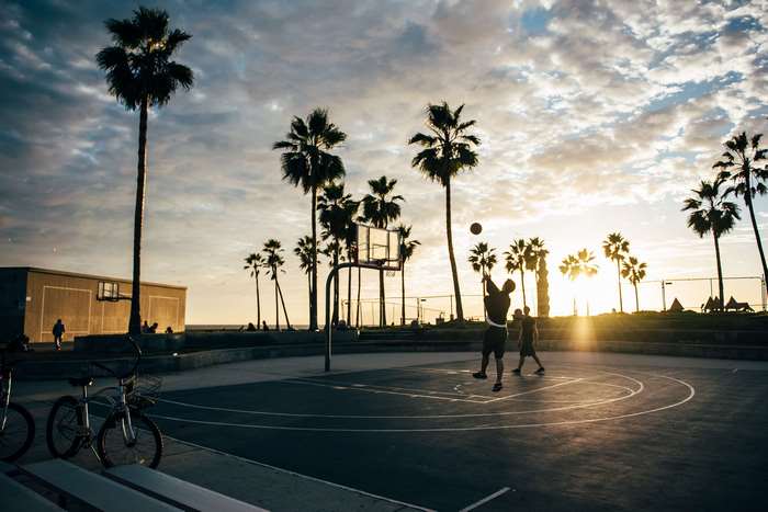 People playing basketball on a court with palm trees at sunset