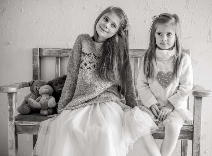 Two young girls sitting on a bench with teddy bears