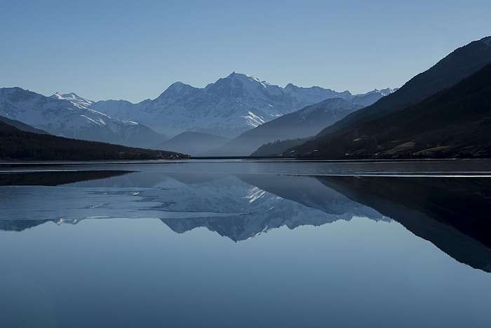 Snow-capped mountains reflected in a calm lake under a clear blue sky