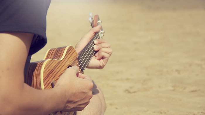 Person playing ukulele on a sandy beach