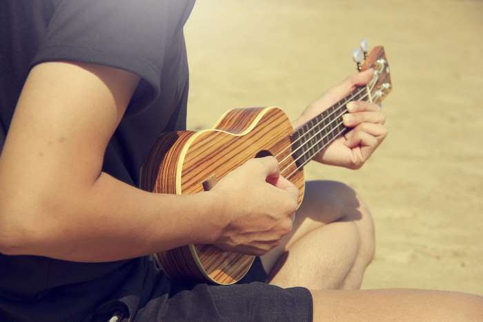 Person playing a ukulele outdoors on sand