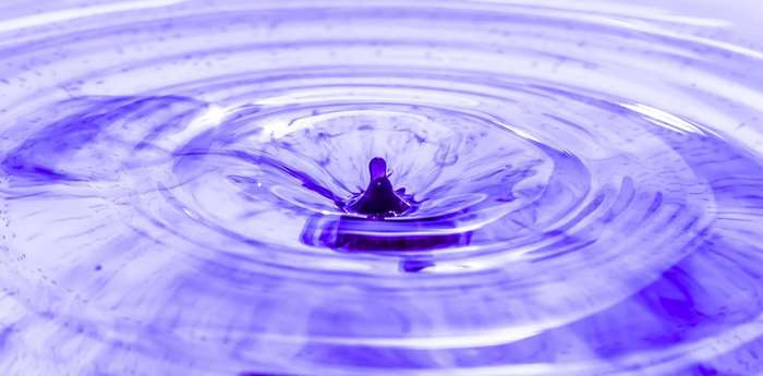 Purple ink drop impacting water surface with ripples