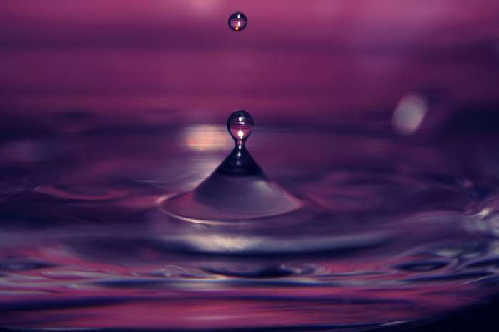 Water drop falling into purple liquid with ripples