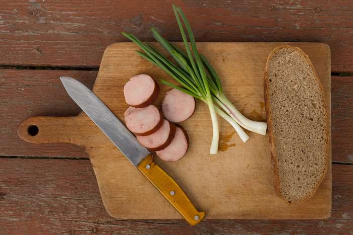 Sausage, green onions, and bread on a chopping board with a knife