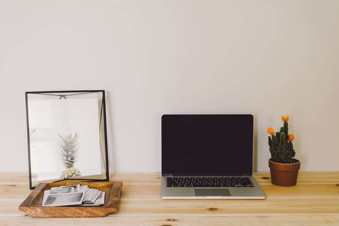 Laptop, framed pineapple art, and cactus on a wooden desk
