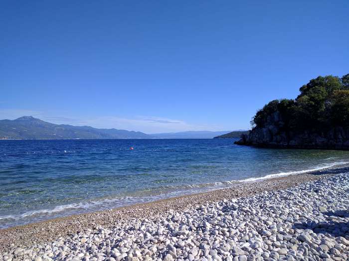 Pebble beach with clear blue sea and distant mountains