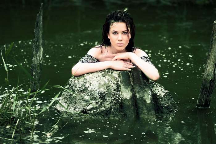 Young woman posing in murky water with a rock