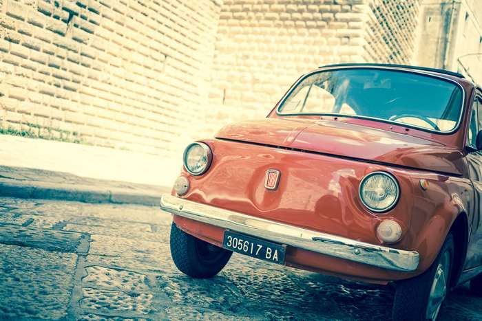 Red Fiat 500 car parked on a cobblestone street in Italy
