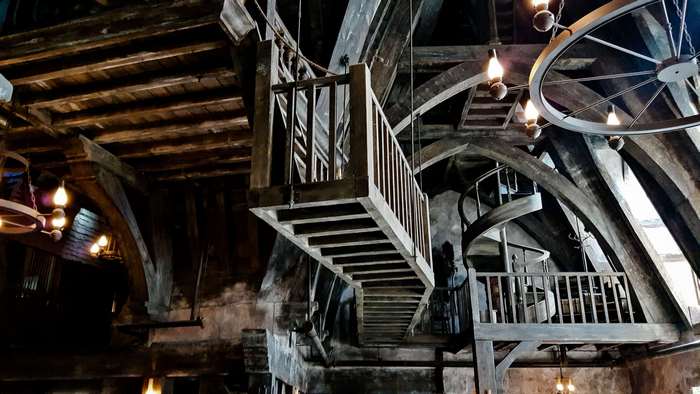 Interior of a medieval-style building with wooden stairs and chandeliers