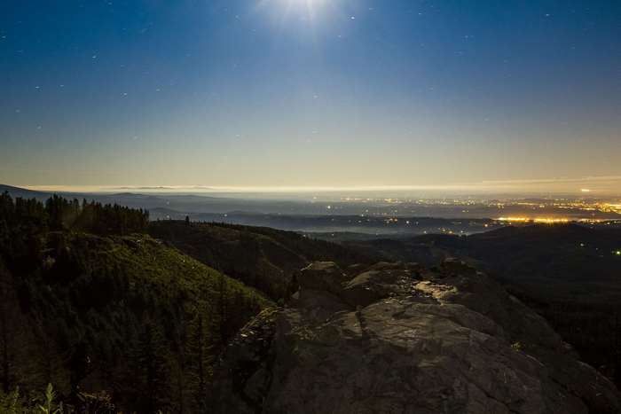 Night sky over city lights and forested hills