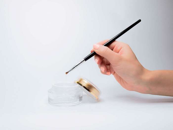 Hand holding brush with gel from cosmetic jar