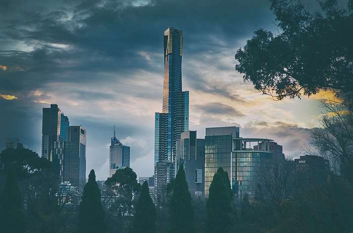 City skyline with skyscrapers and trees under cloudy sky