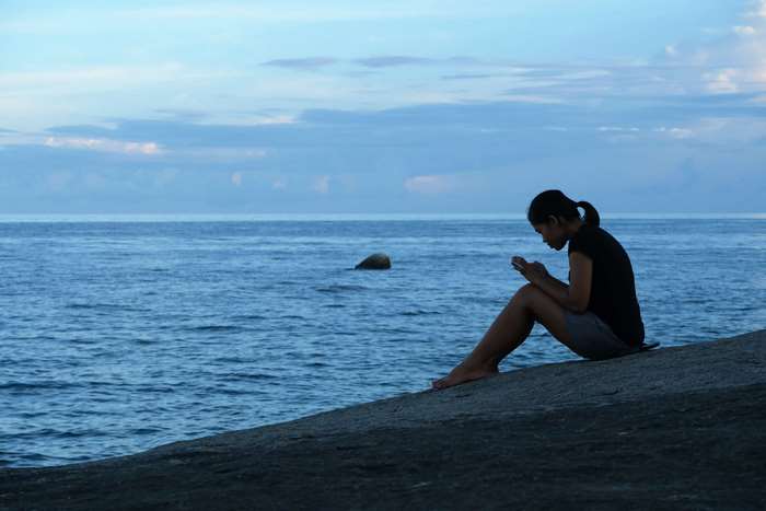Girl on rock by the sea with mobile phone 4K