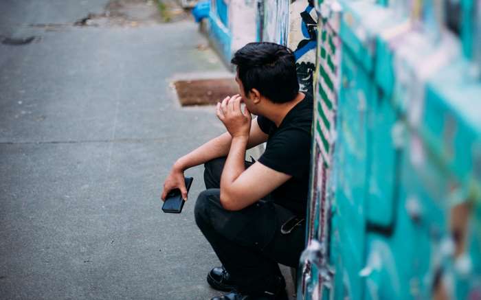 Man sitting by graffiti wall with smartphone