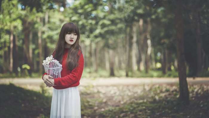 Young woman in red sweater holding a birdcage with flowers