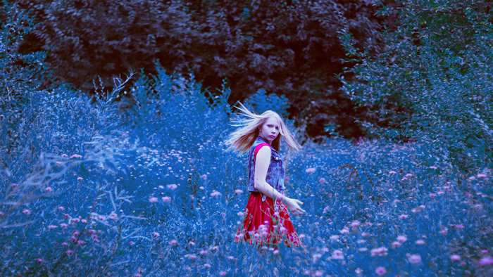 Girl in red skirt and denim vest in a field of flowers