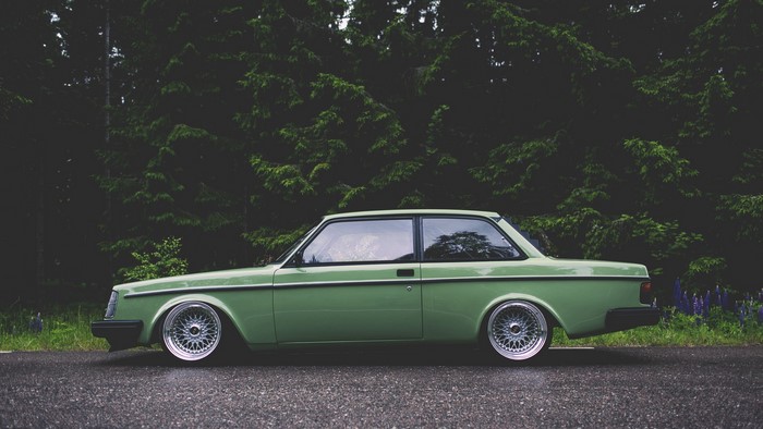 Green Volvo 242 parked by a forest