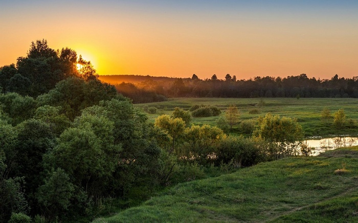 Sunset over a green landscape with trees and a river
