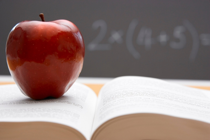 Red apple on an open book with math on blackboard
