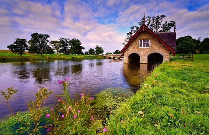 Stone boathouse on a lake with trees and bridge