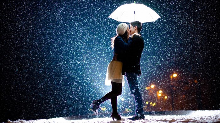 Couple kissing under umbrella in snow