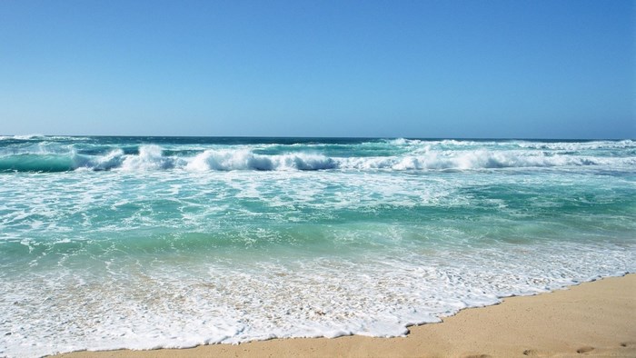 Ocean waves crashing on a sandy beach under a clear blue sky