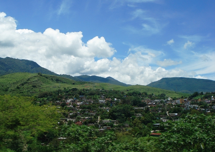 Town nestled in green hills under a blue sky with clouds
