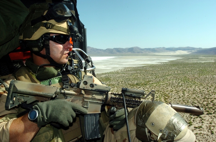 Soldier with rifle in helicopter over desert landscape