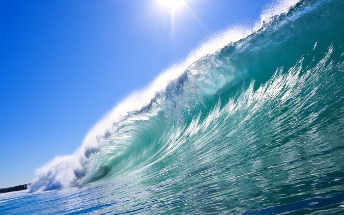 A large ocean wave crests under a bright sun