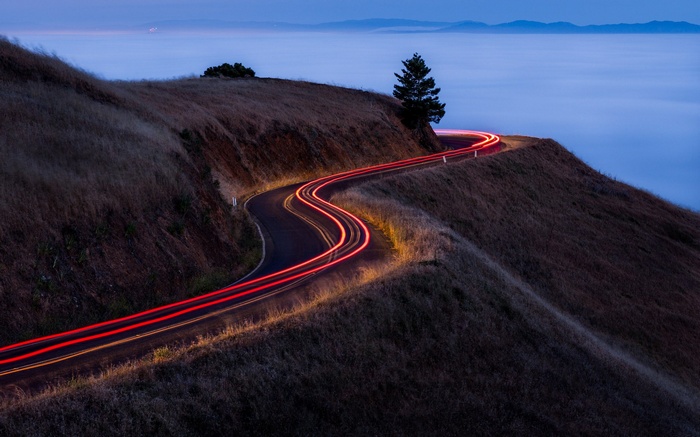 Winding road with light trails over foggy landscape