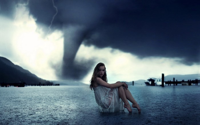 Girl in white dress sits in flooded area with tornado in background
