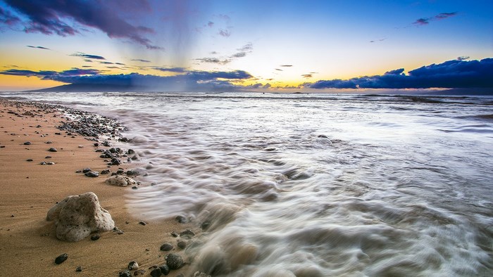 Ocean waves washing onto a pebble beach at sunset