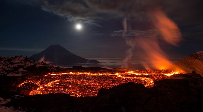 Volcano erupting lava at night with moon