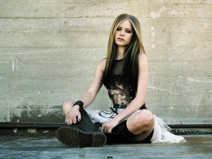 Avril Lavigne sitting by a concrete wall