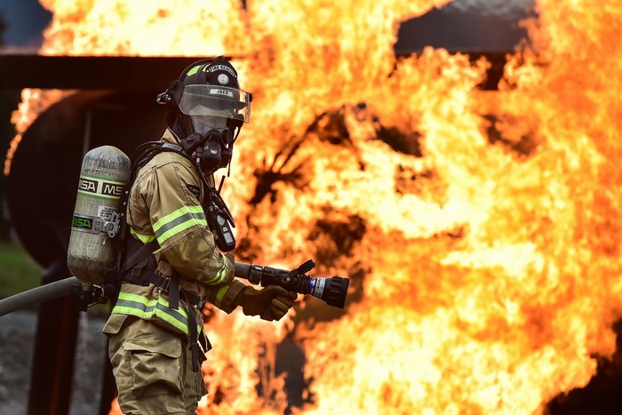 Firefighter in protective gear with a hose near flames