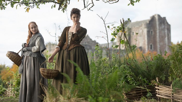 Two women in historical clothing with baskets in front of a castle