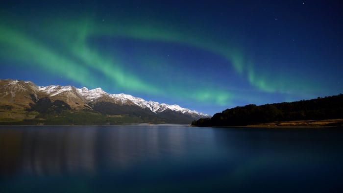 Aurora Borealis over snow-capped mountains and lake