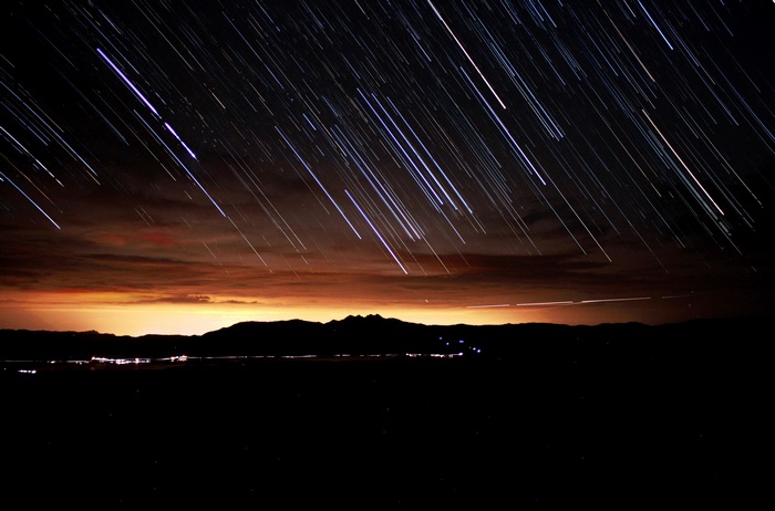 Star trails over mountains and city lights at night