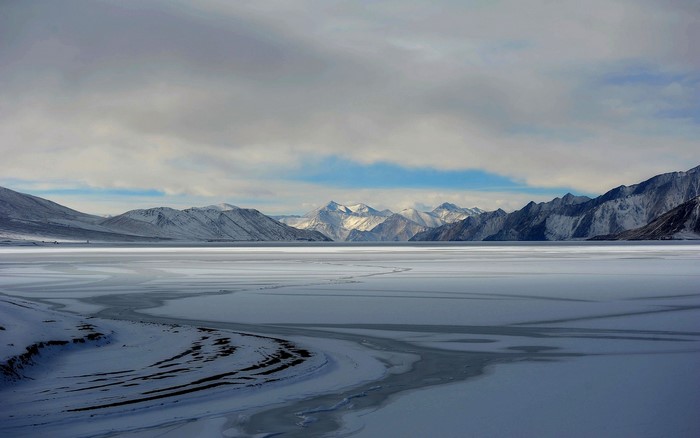 Frozen lake and snow-capped mountains under cloudy sky