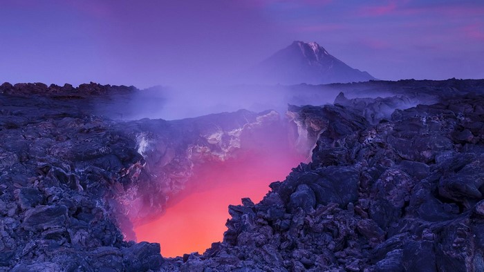 Volcano crater with lava and distant mountain at dusk